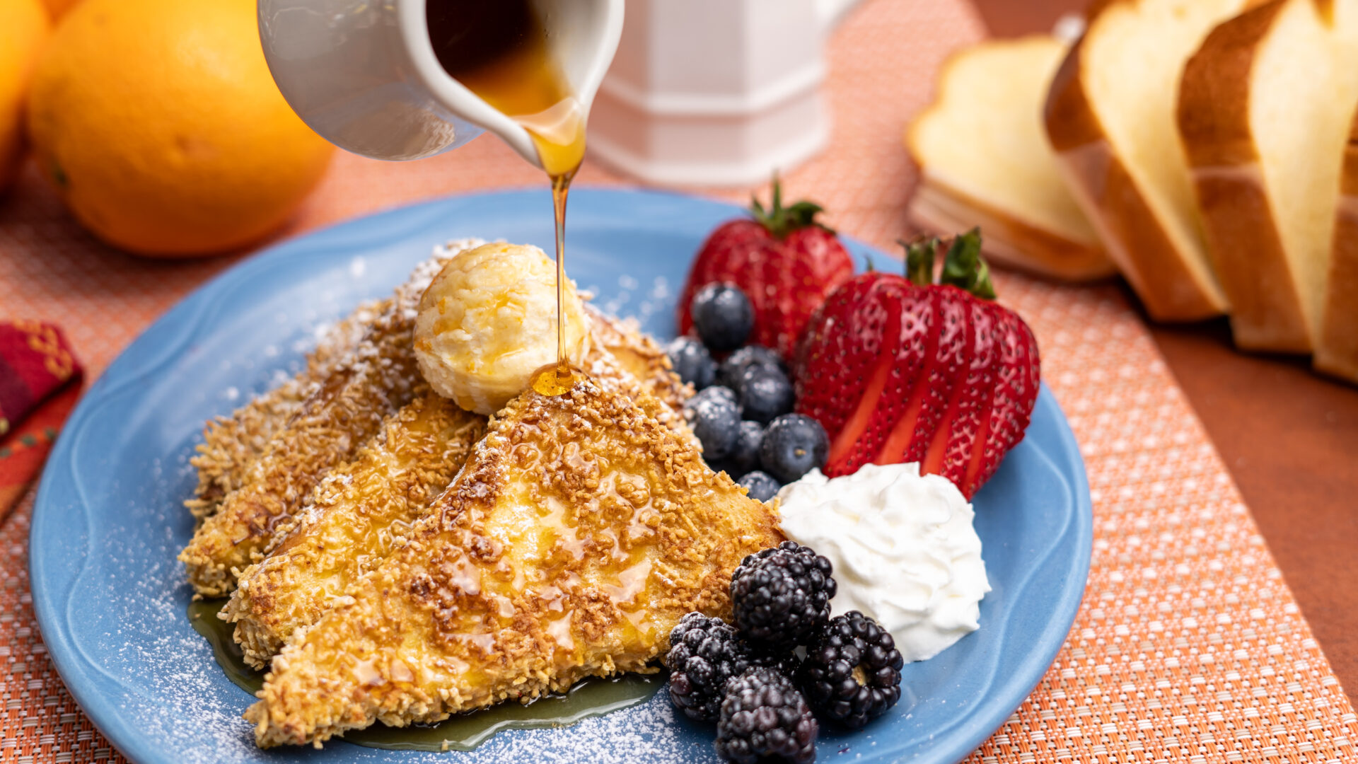 Warm maple syrup being poured onto French Toast with a dollop of orange mascarpone cream and fresh berries