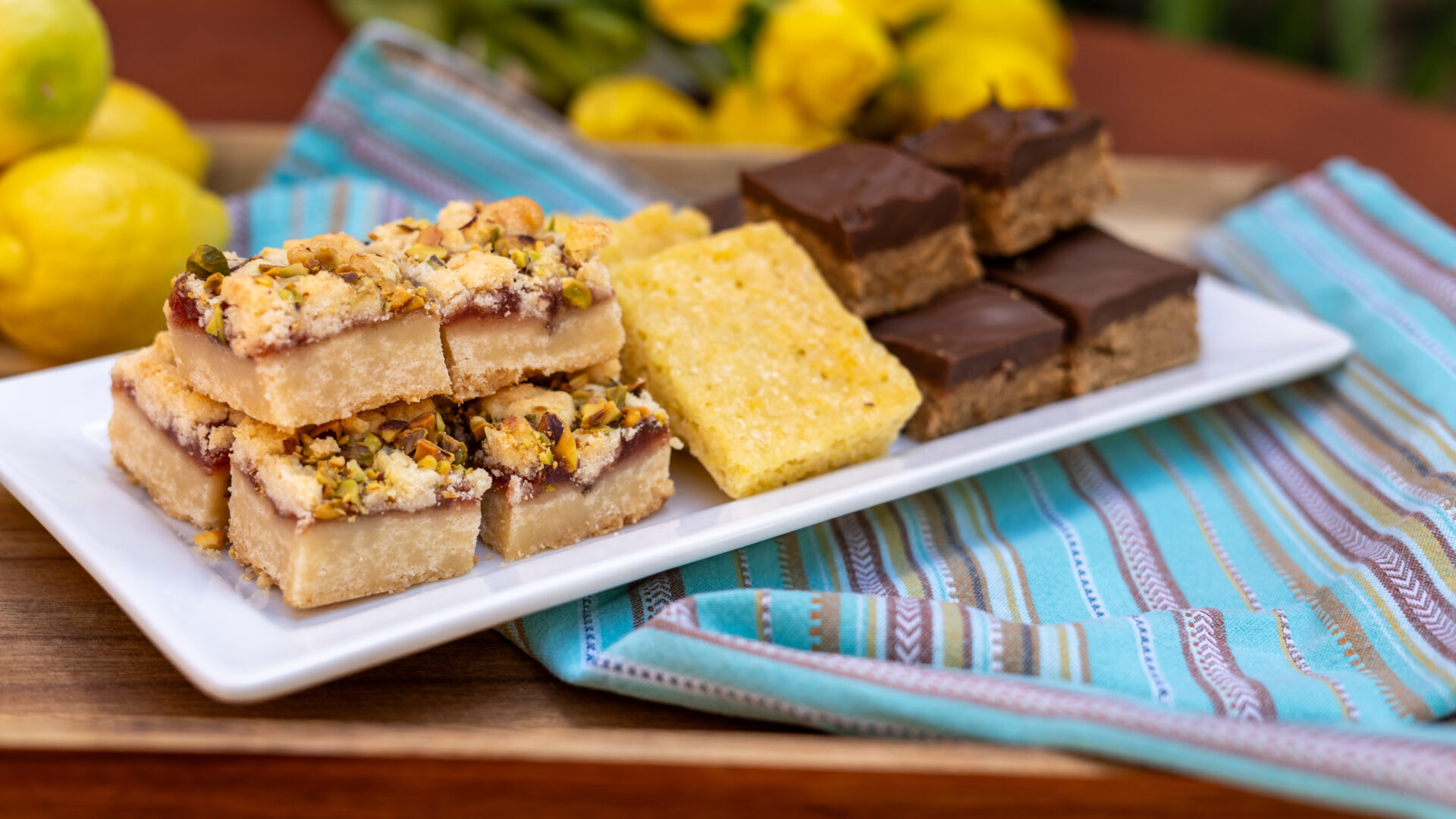 A white tray with cut baked bars including strawberry cardamon pistachio, lemon brownies, and Scotcharoos.