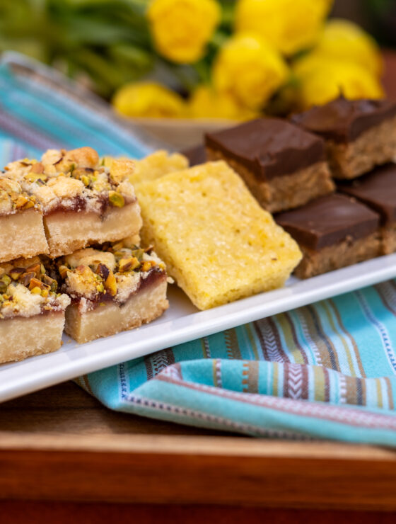 A white tray with cut baked bars including strawberry cardamon pistachio, lemon brownies, and Scotcharoos.