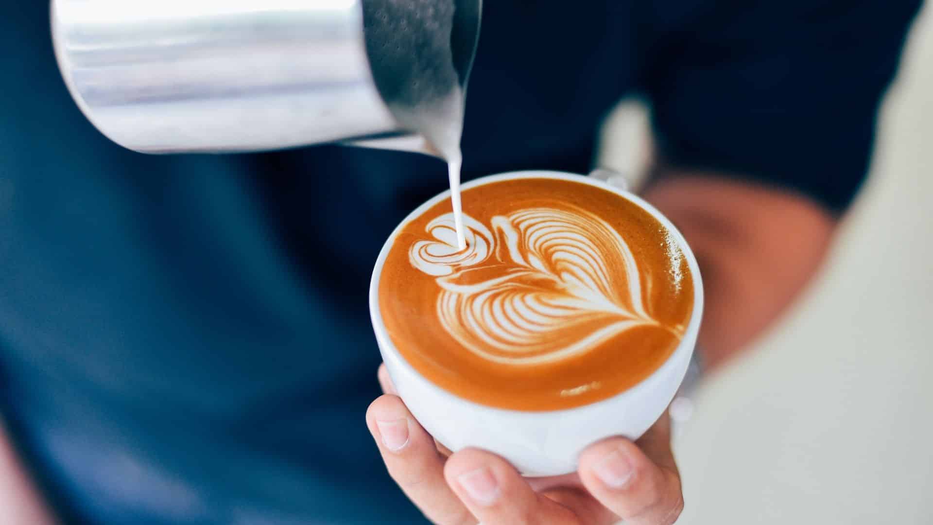 a barista pouring milk into a latte to make latte art 