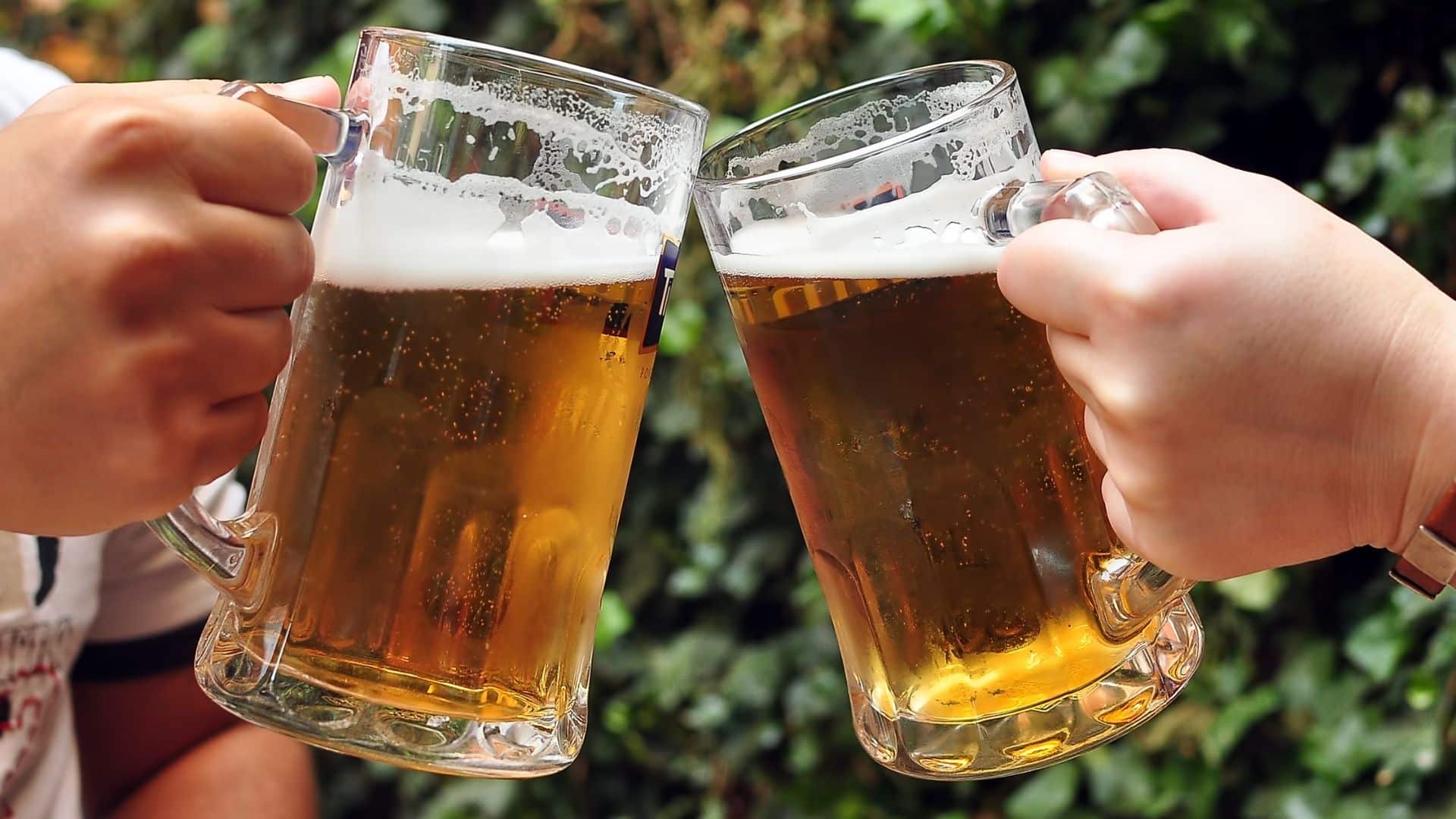 two people hold mugs of beer up for a cheers on an outdoor patio 